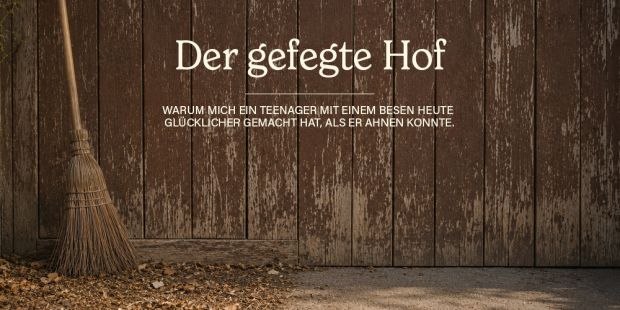 Ein Besen vor einem alten, braunen Scheunentor, der Boden ist auf einer Seite gefegt, auf der anderen Seite liegen vertrocknet Blätter.